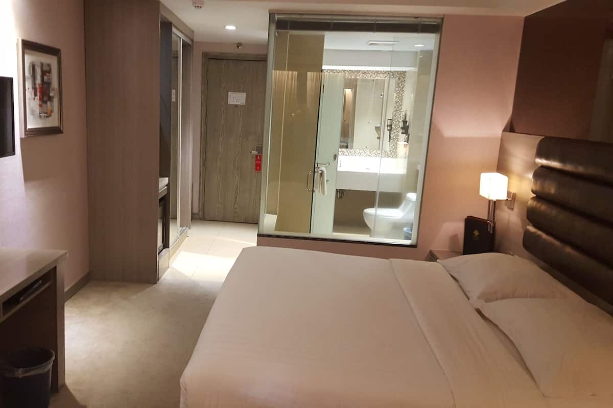 Une chambre d’hôtel équipée d’un lit, d’un bureau, d’une télévision et d’une salle de bain visible à travers une porte en verre.