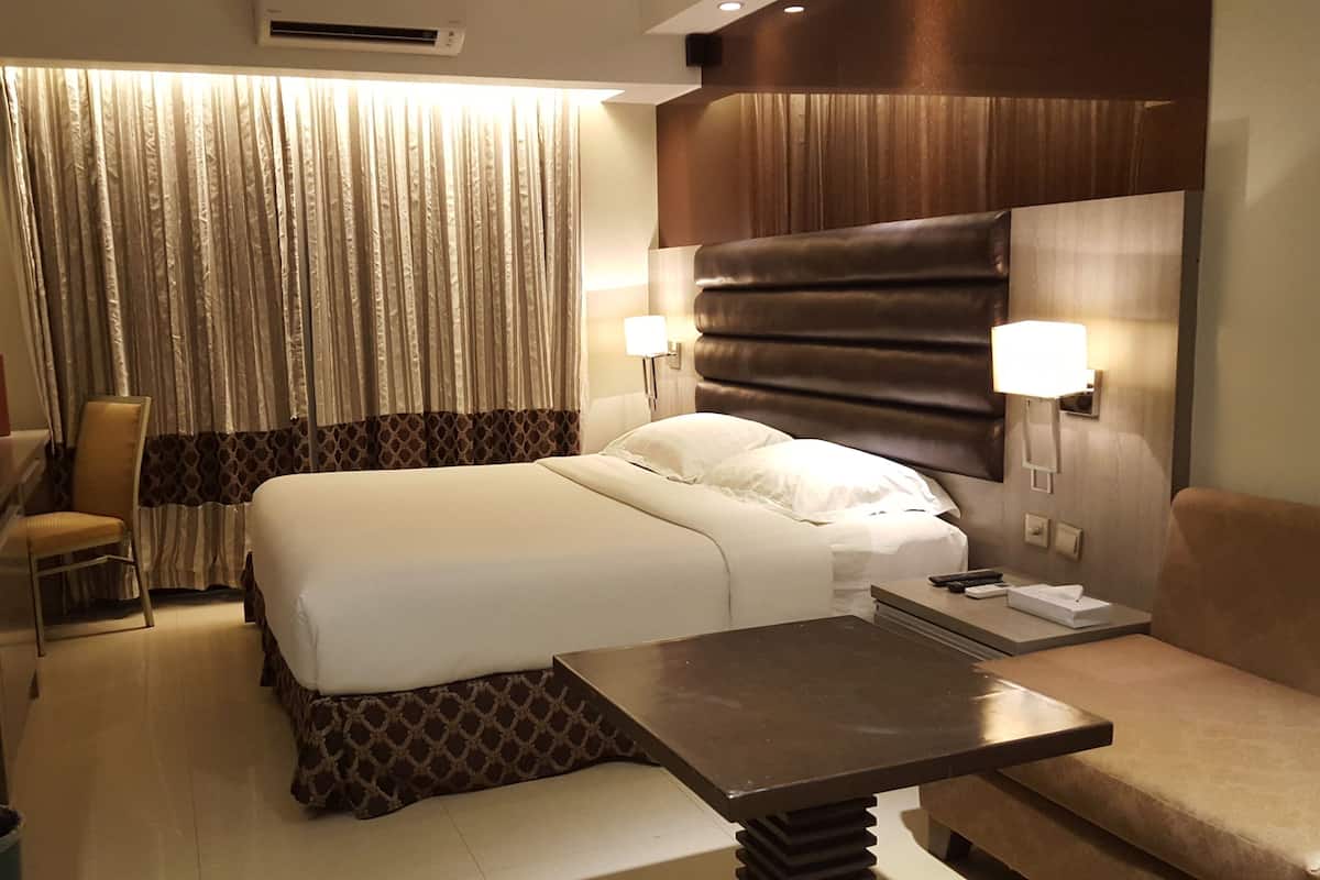 Une chambre d’hôtel avec un lit, des tables de chevet, une chaise, un bureau et une lampe.