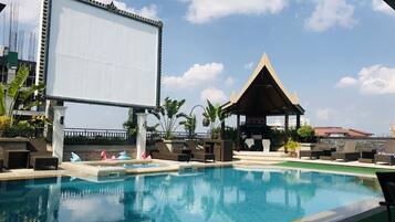 A pool area with lounge chairs, a large screen, and a gazebo.