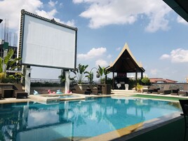 A pool area with lounge chairs, a large screen, and a gazebo.