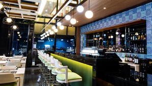 A modern bar area with a long counter, bar stools, and a variety of bottles. - Prime Asia Hotel (Angeles City)