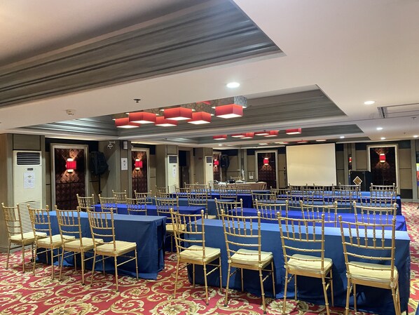 A conference room with rows of tables and chairs, a projector screen, and a patterned carpet.