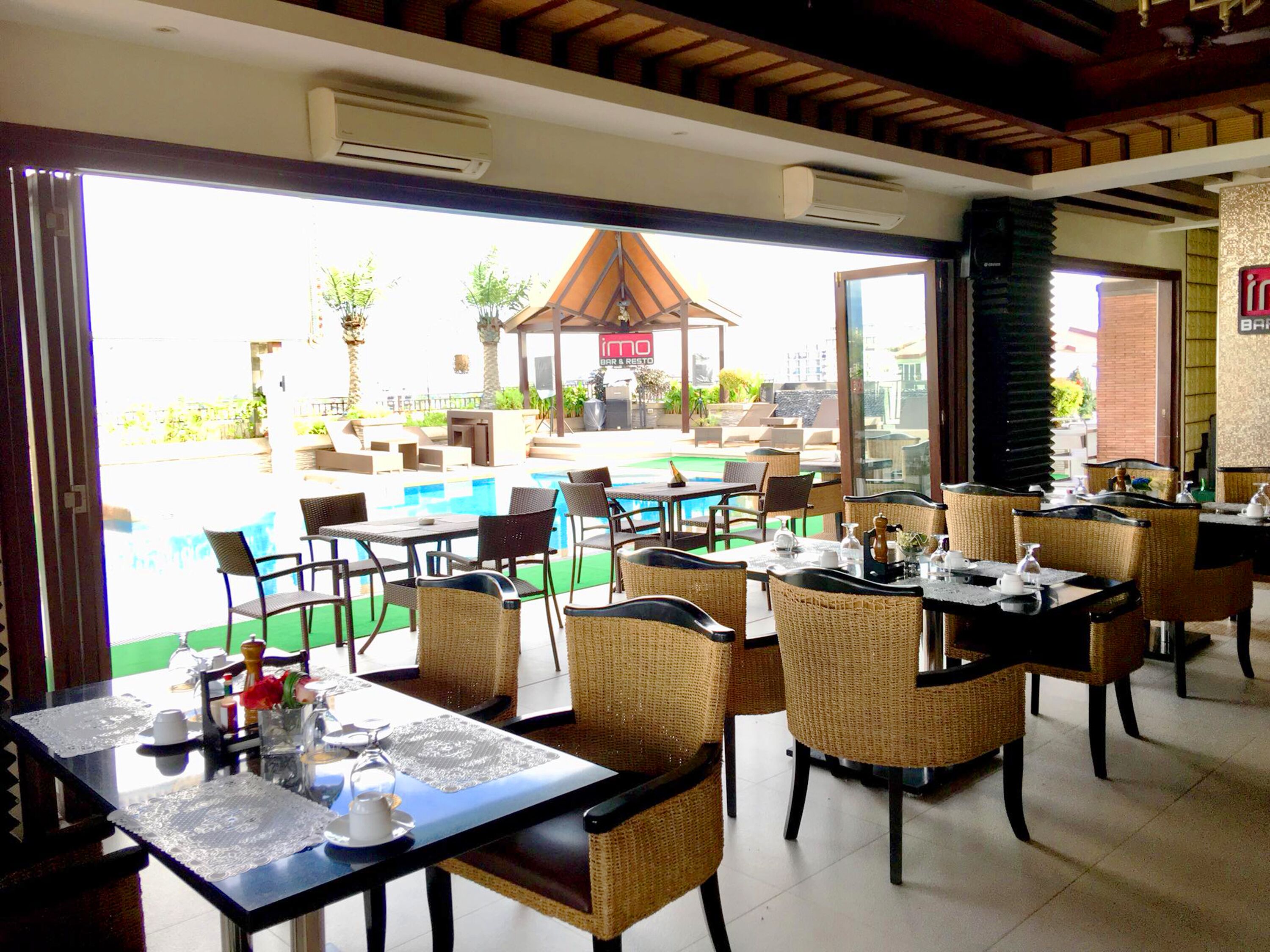 A restaurant with outdoor seating overlooking a pool and garden area.