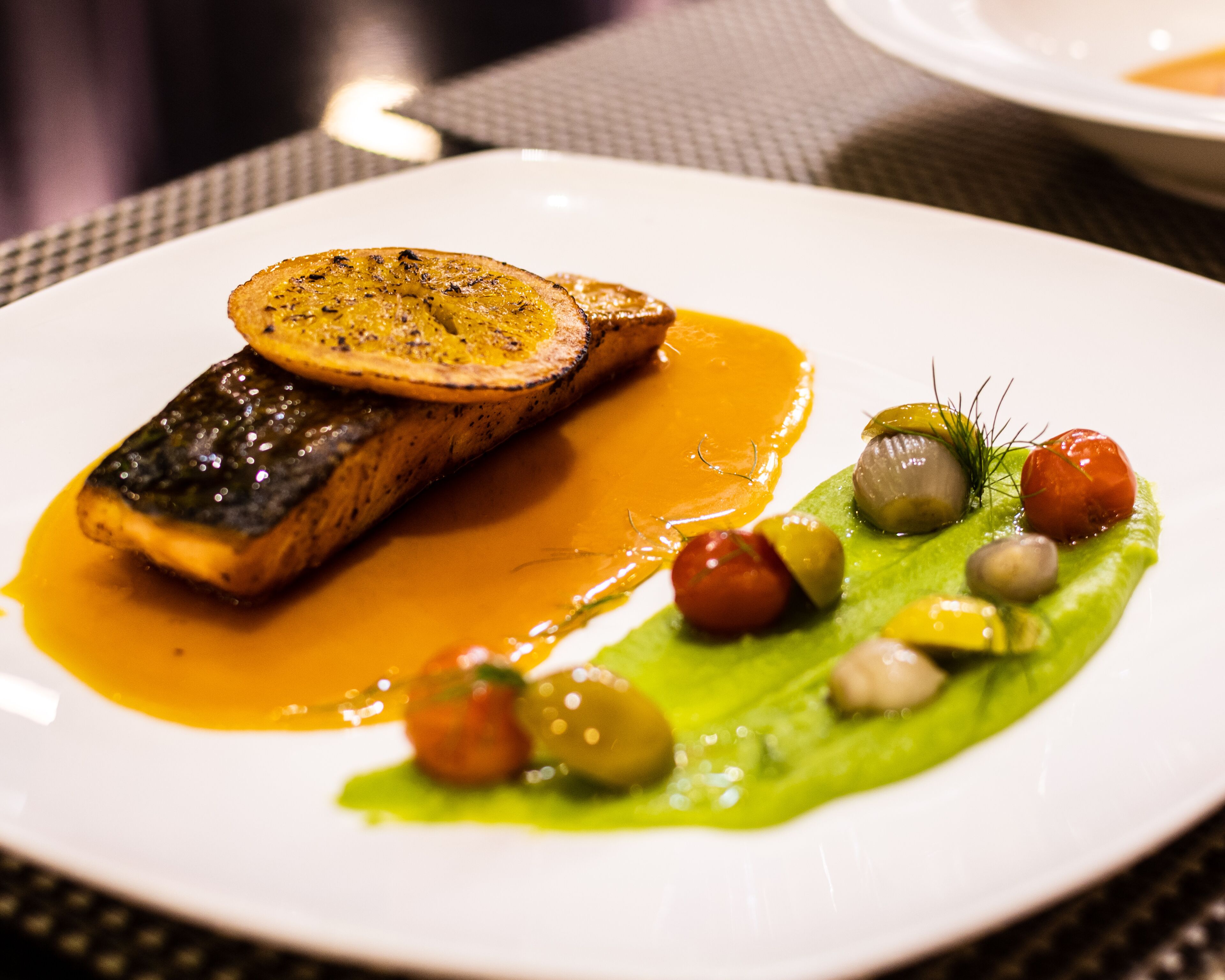 Un plato de comida con un filete de pescado, rodajas de patata y un vegetal verde con bolitas.
