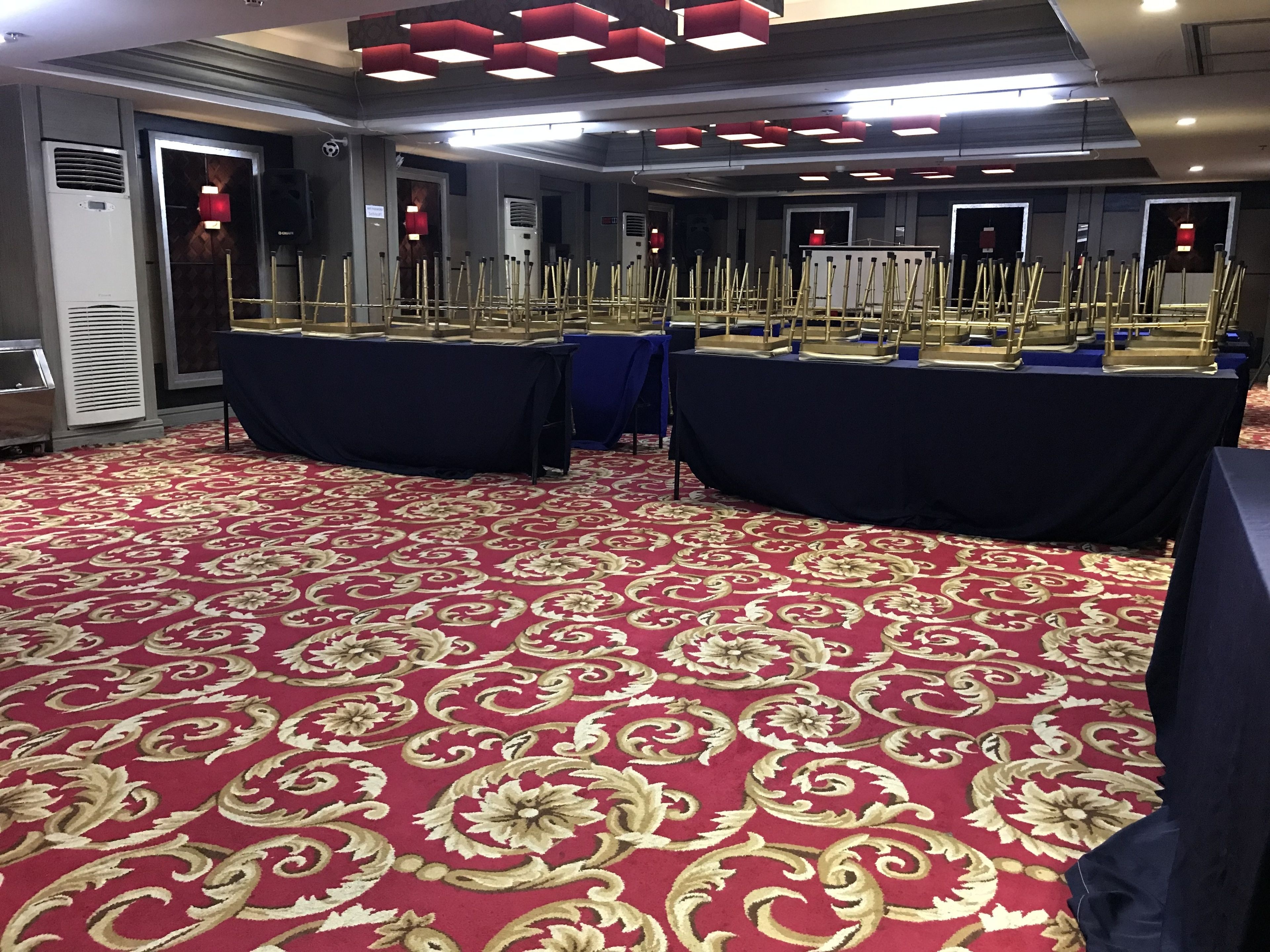 Een congreszaal met een tapijt met een rood patroon, tafels met blauwe tafelkleden en rode sfeerverlichting.