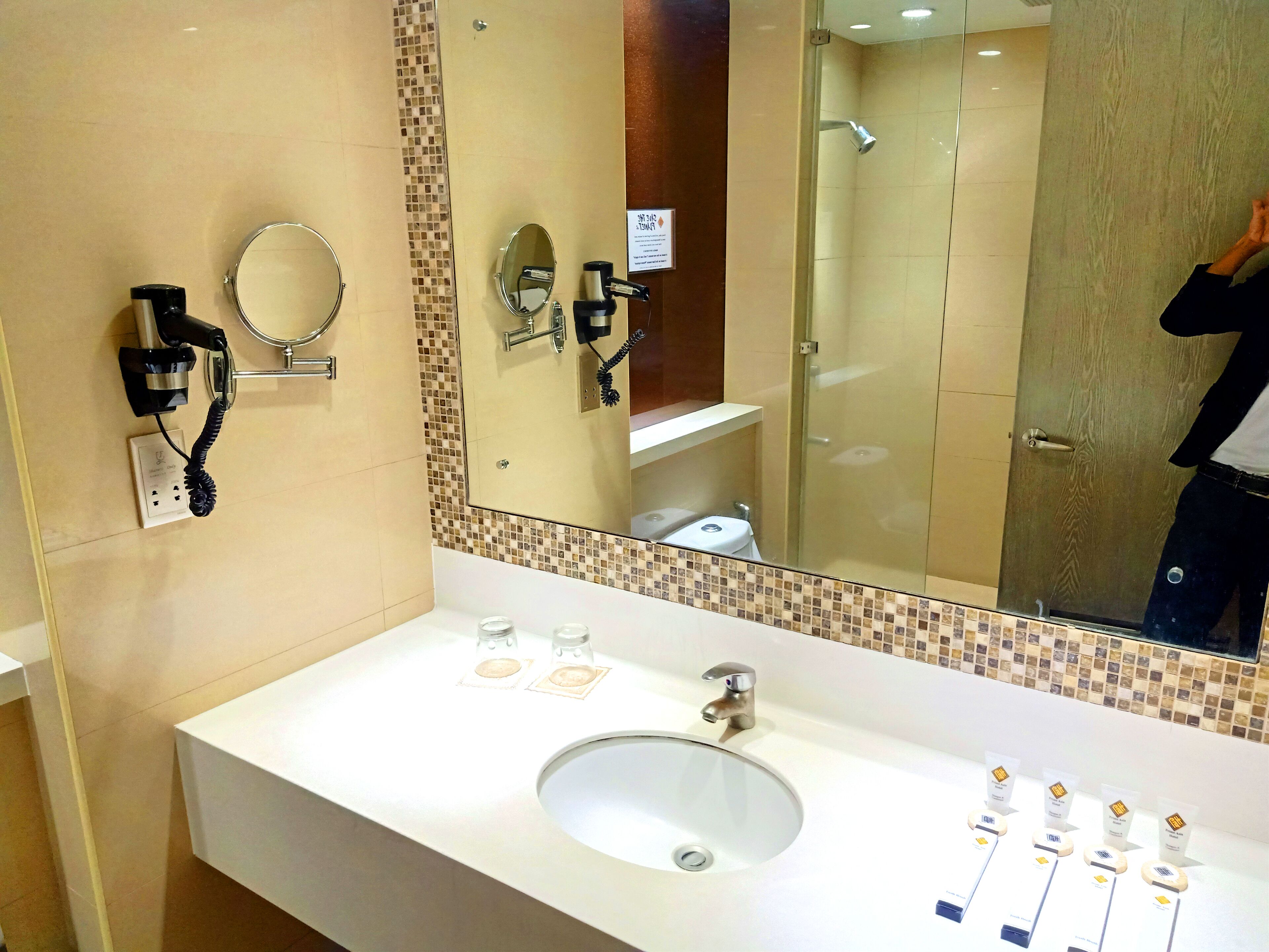 Un baño de hotel con un espejo grande, un lavamanos, un secador de pelo y una ducha.