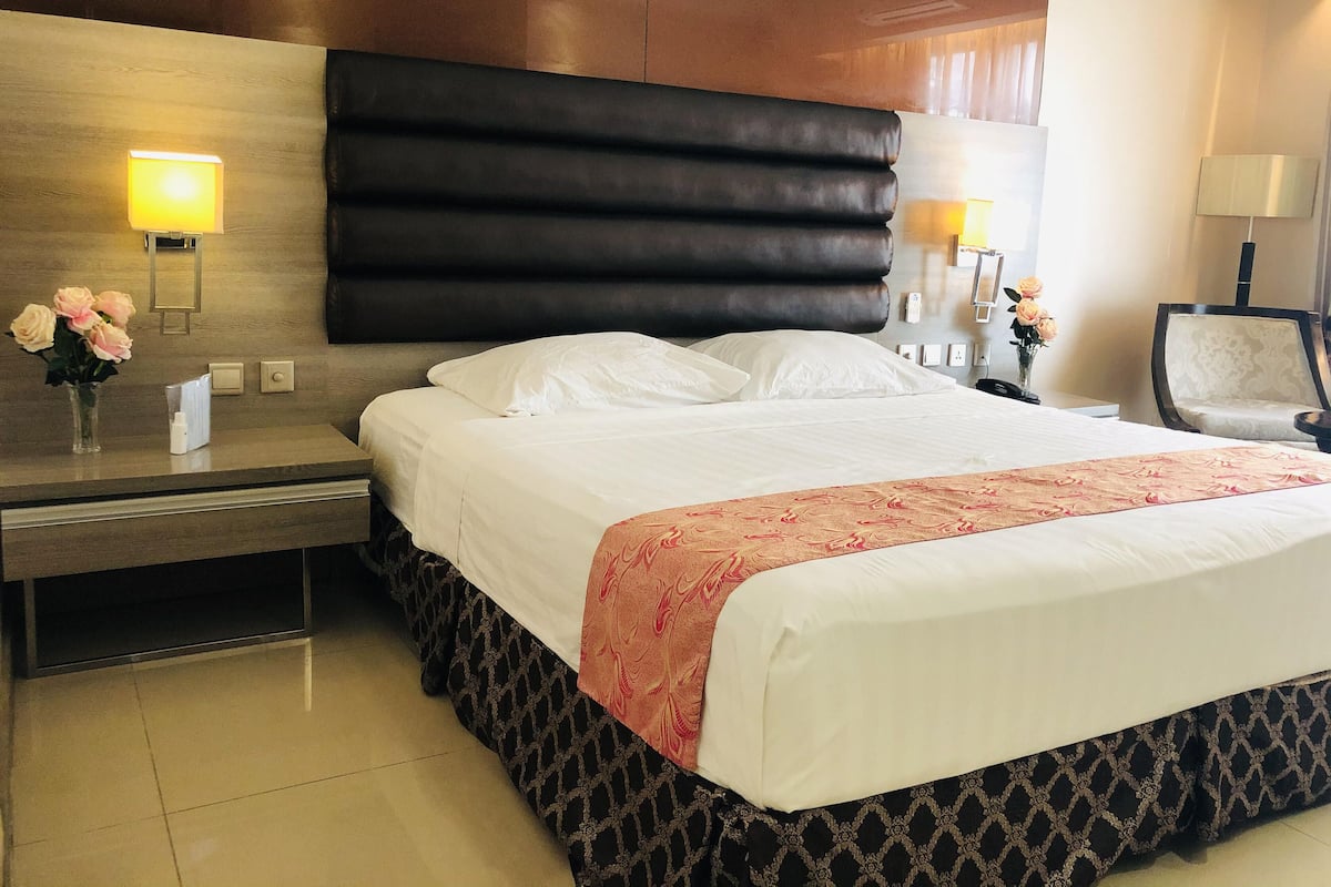Une chambre d’hôtel avec un grand lit, une table de chevet, une lampe fixée au mur et une chaise.