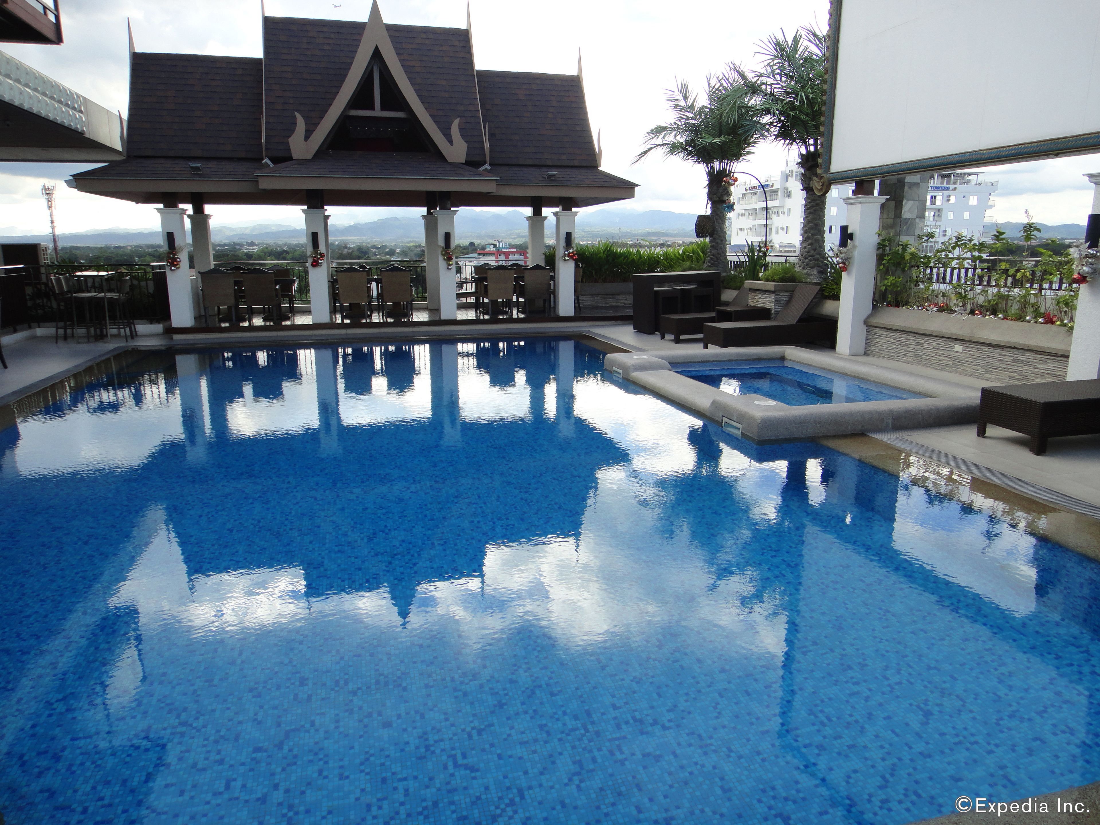 Une piscine dotée d’une terrasse carrelée, de chaises longues et d’un espace salon couvert agrémenté d’un toit décoratif.