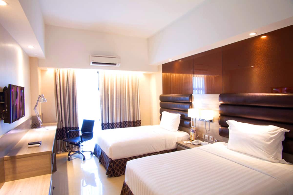 Une chambre d’hôtel avec deux lits, un bureau, une chaise, une télévision et un appareil de climatisation.