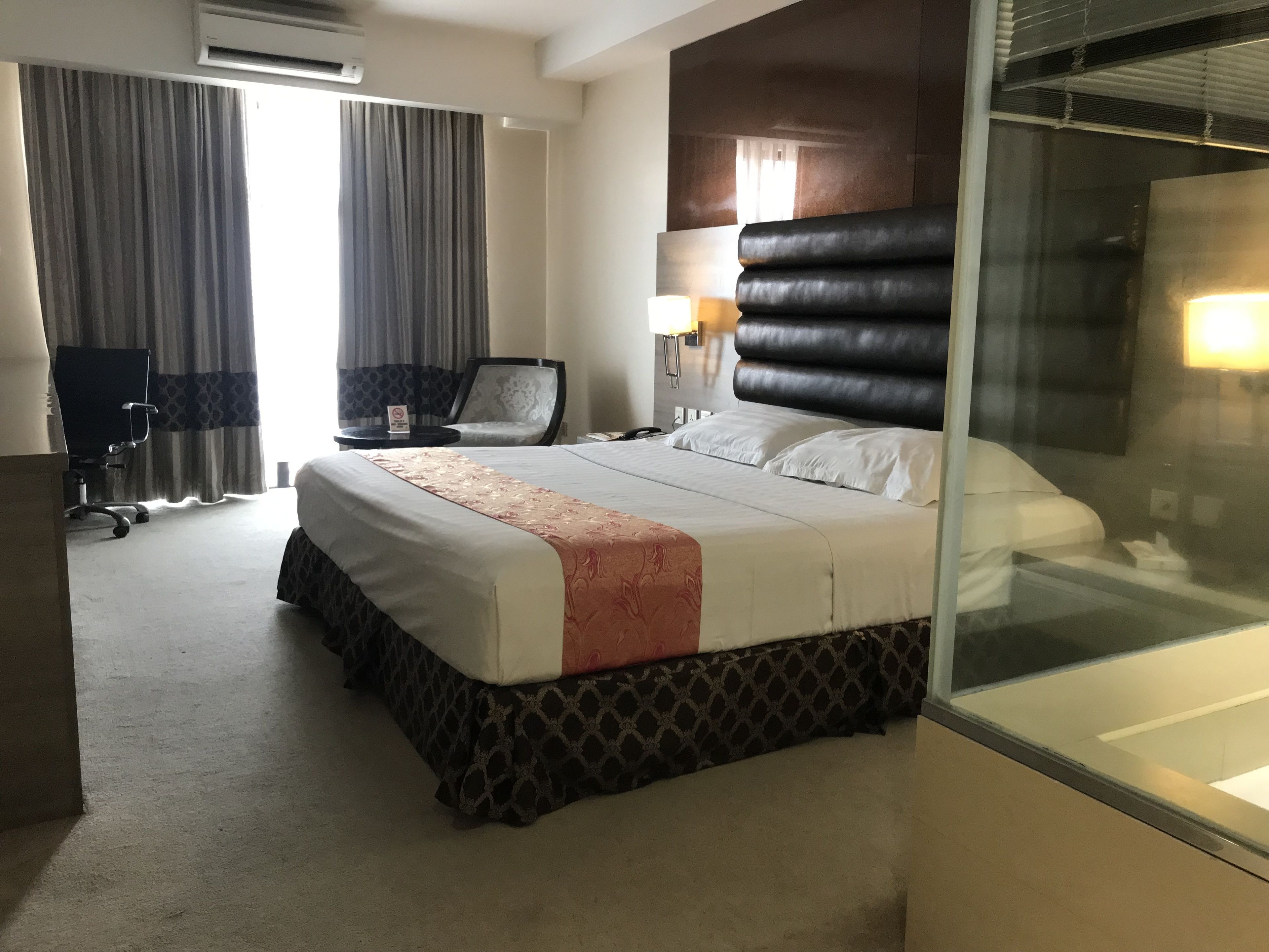 Une chambre d’hôtel avec un grand lit, un bureau, une chaise et une cloison en verre.