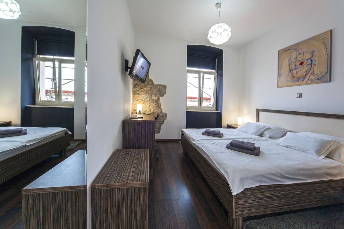 A modern bedroom with two beds, a stone accent wall, a mounted TV, and a large abstract painting.