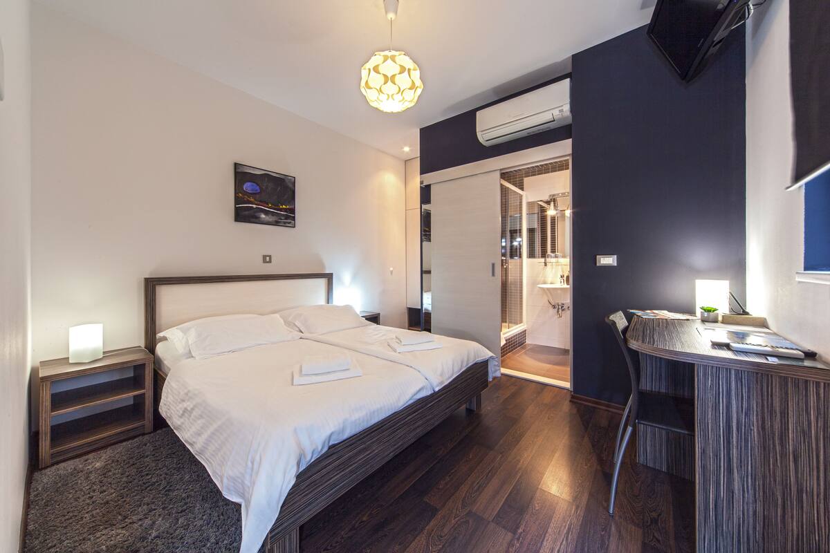 A modern bedroom with a large bed, bedside tables, a desk, and a hanging light fixture.