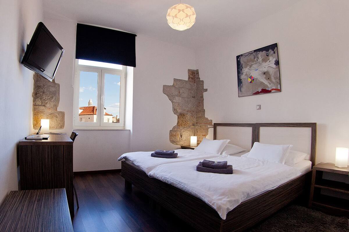 A bedroom with a bed, a desk, a TV, a window with a view, and a map on the wall.