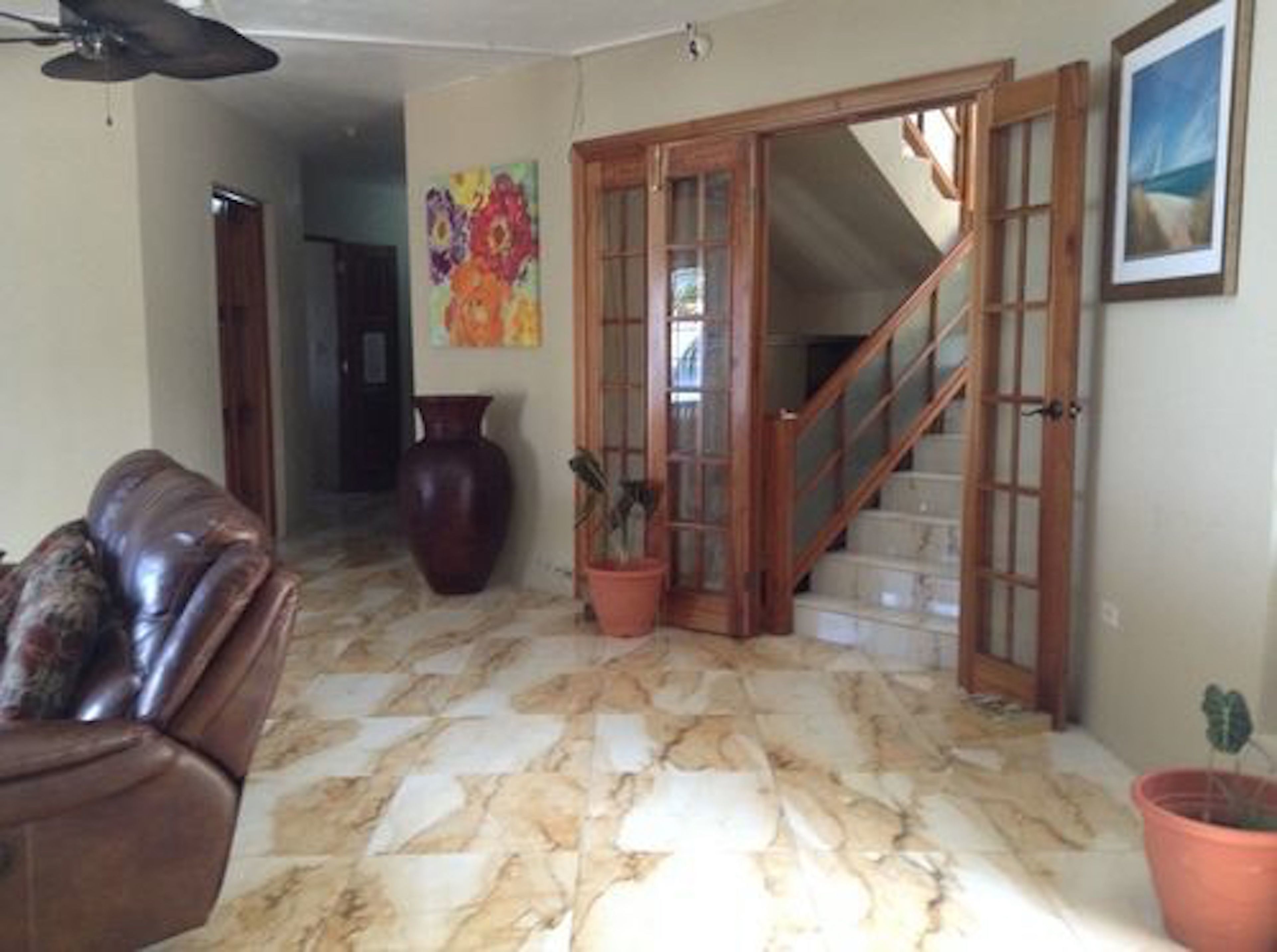 A living room with a marble floor, a brown leather sofa, a large vase, and a staircase leading to another level.