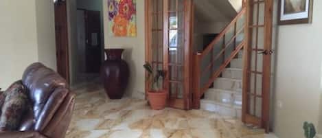 A living room with a marble floor, a brown leather sofa, a large vase, and a staircase leading to another level.