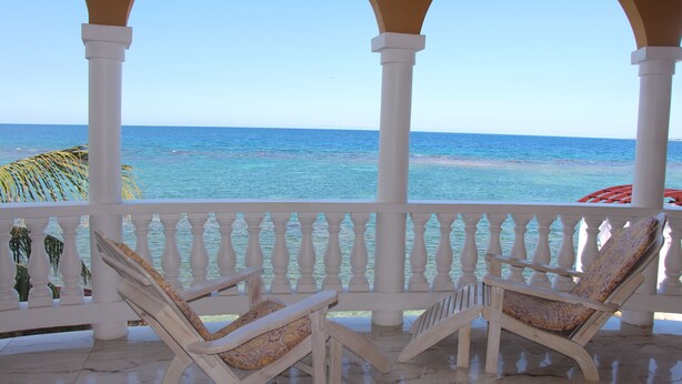 Un espacio al aire libre cubierto con dos sillones de madera y una barandilla blanca con vistas al mar.