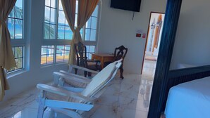 Una habitación con una cama, una silla, una mesa y vistas al mar a través de amplias ventanas.