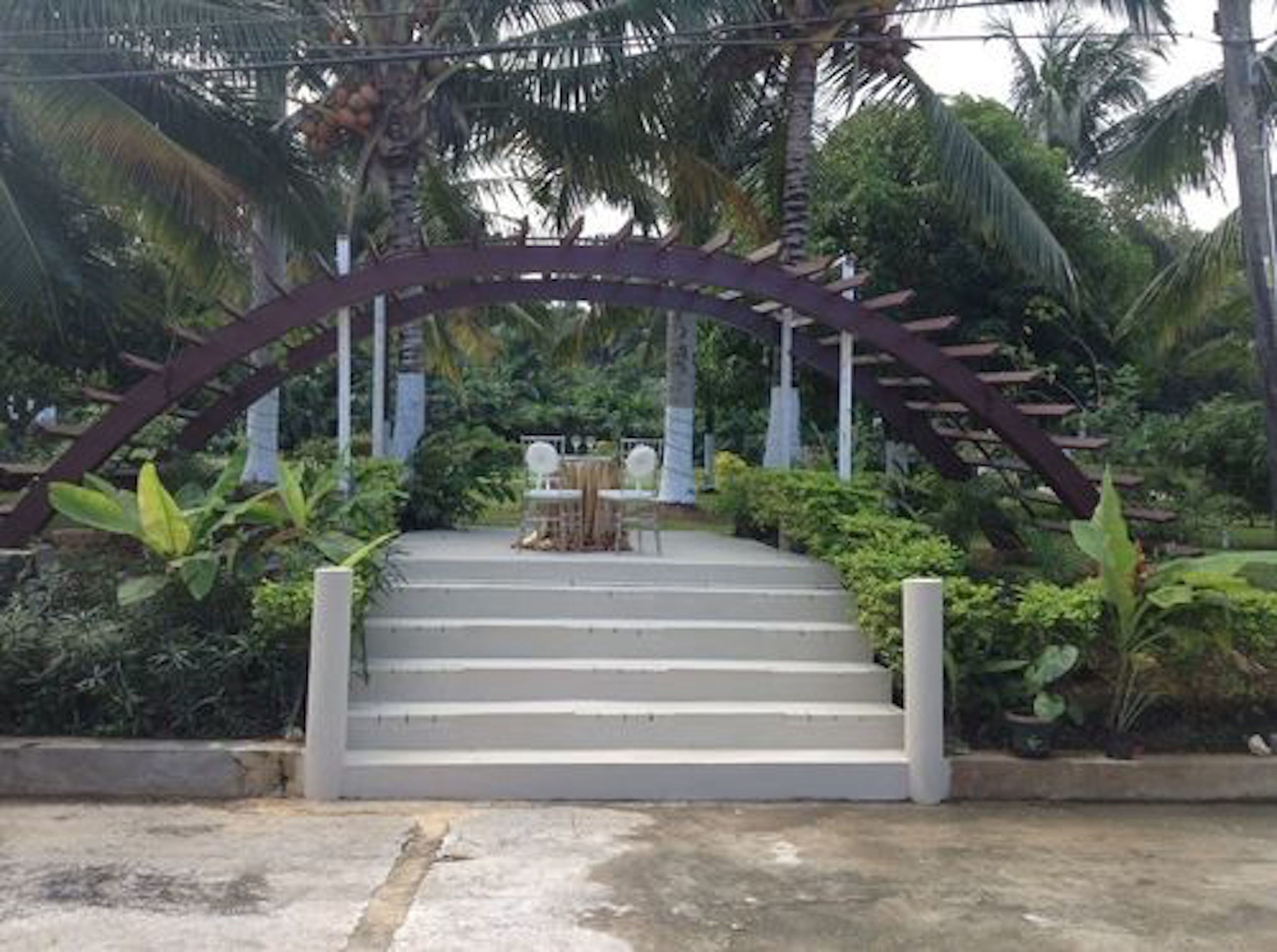 A set of outdoor stairs leading to a covered seating area surrounded by lush greenery and palm trees.