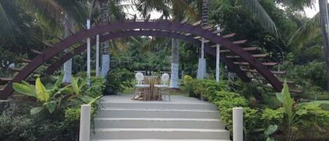 A set of outdoor stairs leading to a covered seating area surrounded by lush greenery and palm trees.