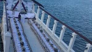 Montaje para una boda al aire libre con mesas y sillas dispuestas a lo largo de un balcón con vista al mar.