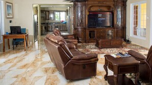 Amplia sala de estar con un sofá grande de cuero, un mueble de entretenimiento de madera y un comedor visible a través de un arco.