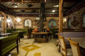Een restaurant met groene, beklede zithoeken, een centrale tafel met fruit en behang met patronen.