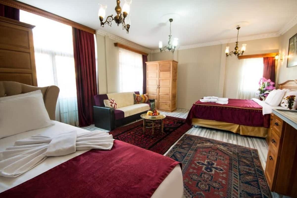 Habitació d'hotel amb dos llits, un sofà, un armari i una taula petita plena de fruita.