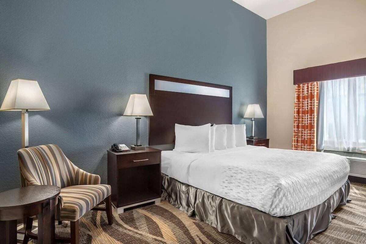 A hotel room with a bed, two bedside tables, a chair, and a lamp.