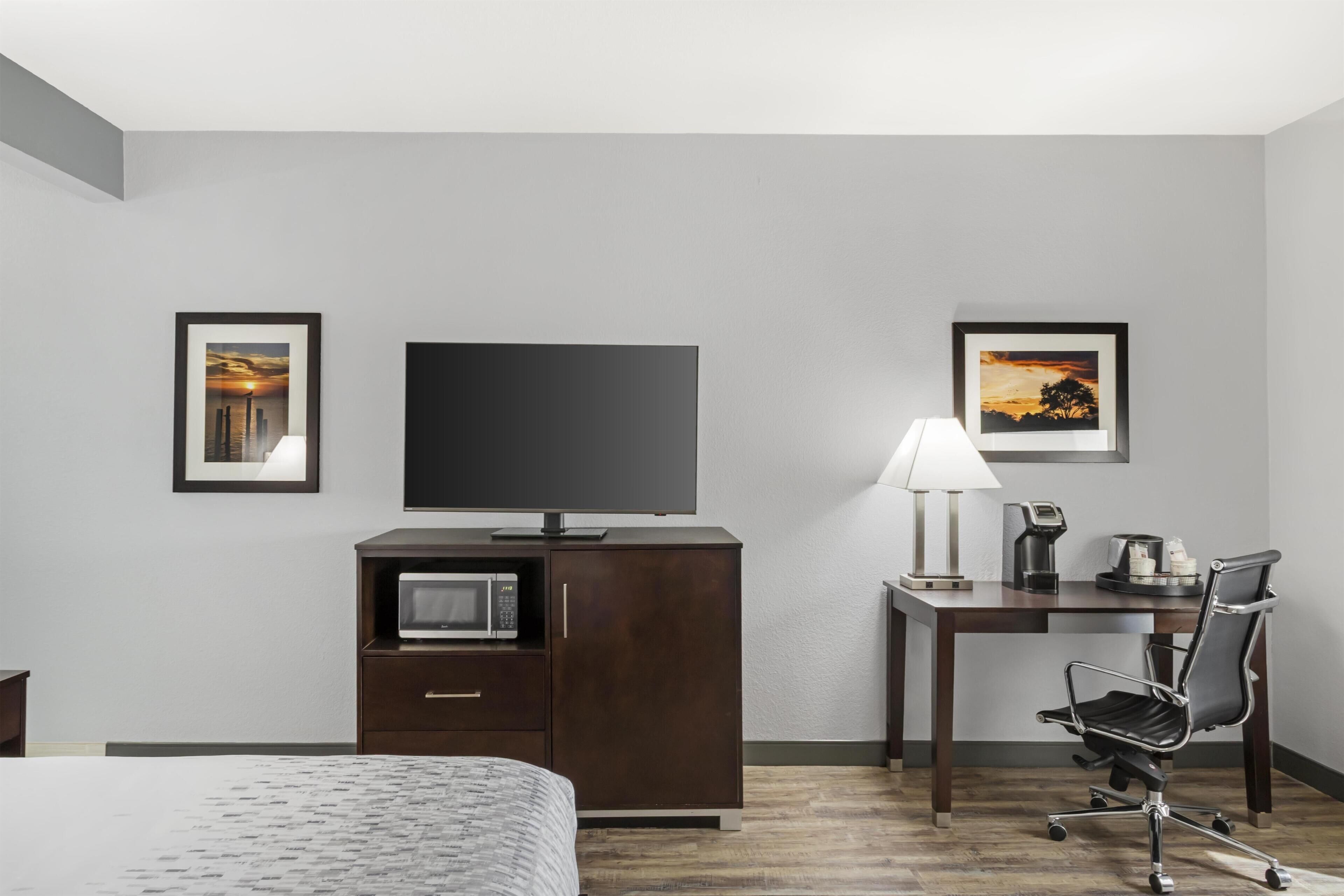 Habitació d'hotel amb llit, televisió, escriptori amb làmpada, cadira i microones.