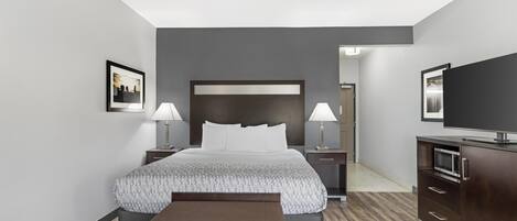 A hotel room with a large bed, two bedside tables with lamps, a bench, a TV, and a microwave.