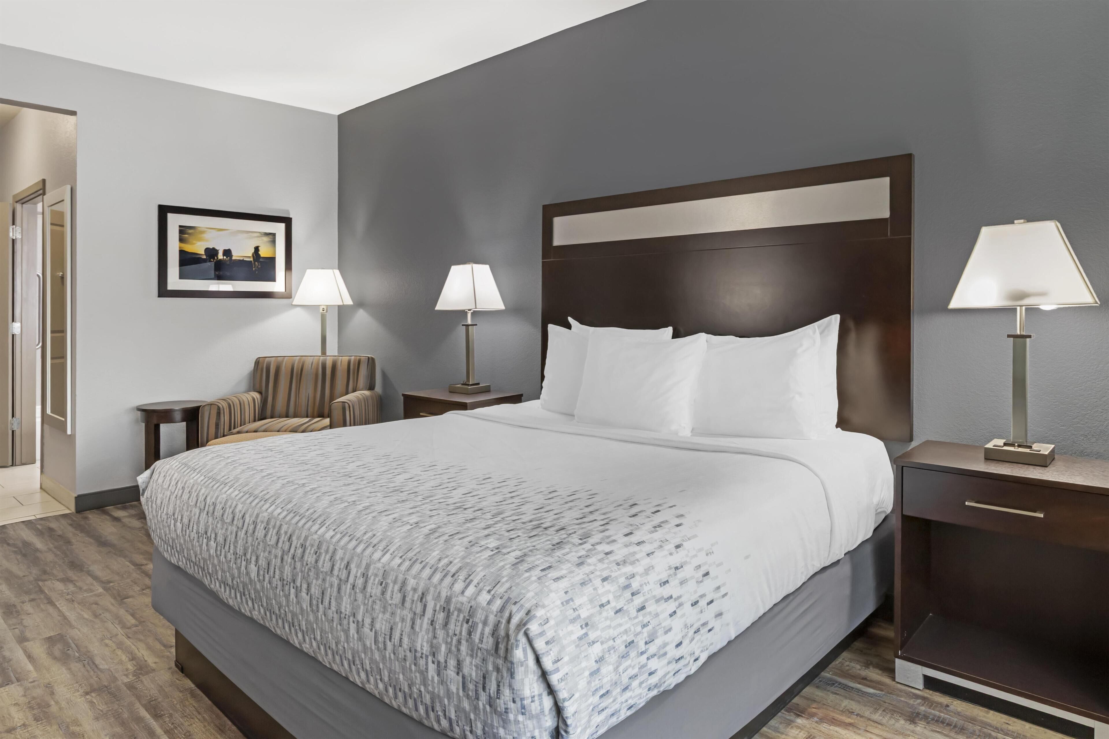 Een hotelkamer met een groot bed, twee nachtkastjes met lampen, een stoel en een lijst met een afbeelding aan de muur.