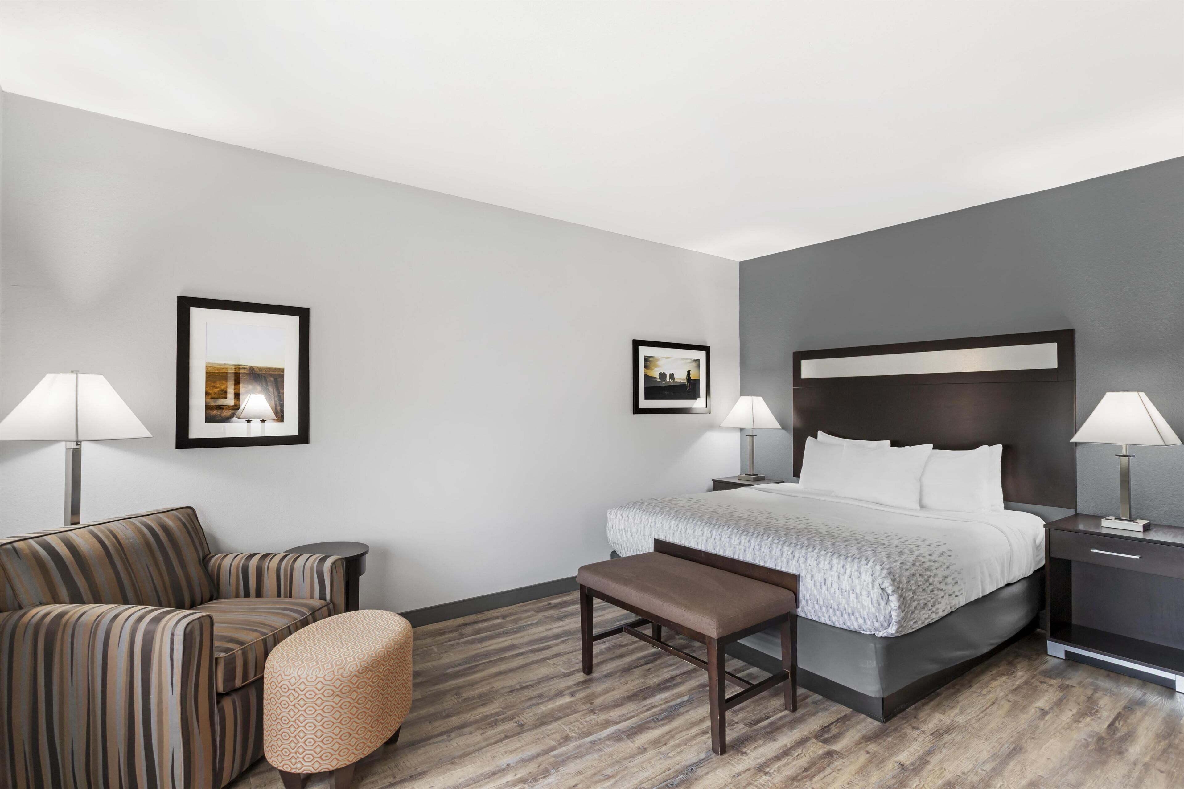 A hotel room with a bed, two bedside tables, a chair, a bench, and two framed pictures on the wall.