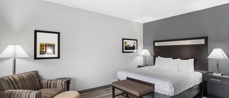 A hotel room with a bed, two bedside tables, a chair, a bench, and two framed pictures on the wall.