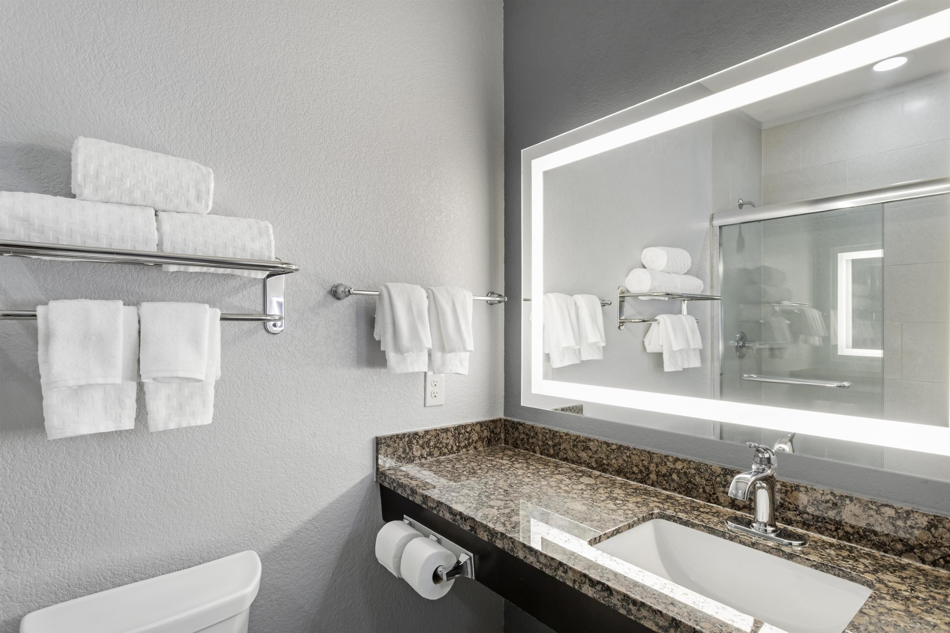 A modern bathroom with a granite countertop sink, a large mirror, and a towel rack with neatly folded towels.