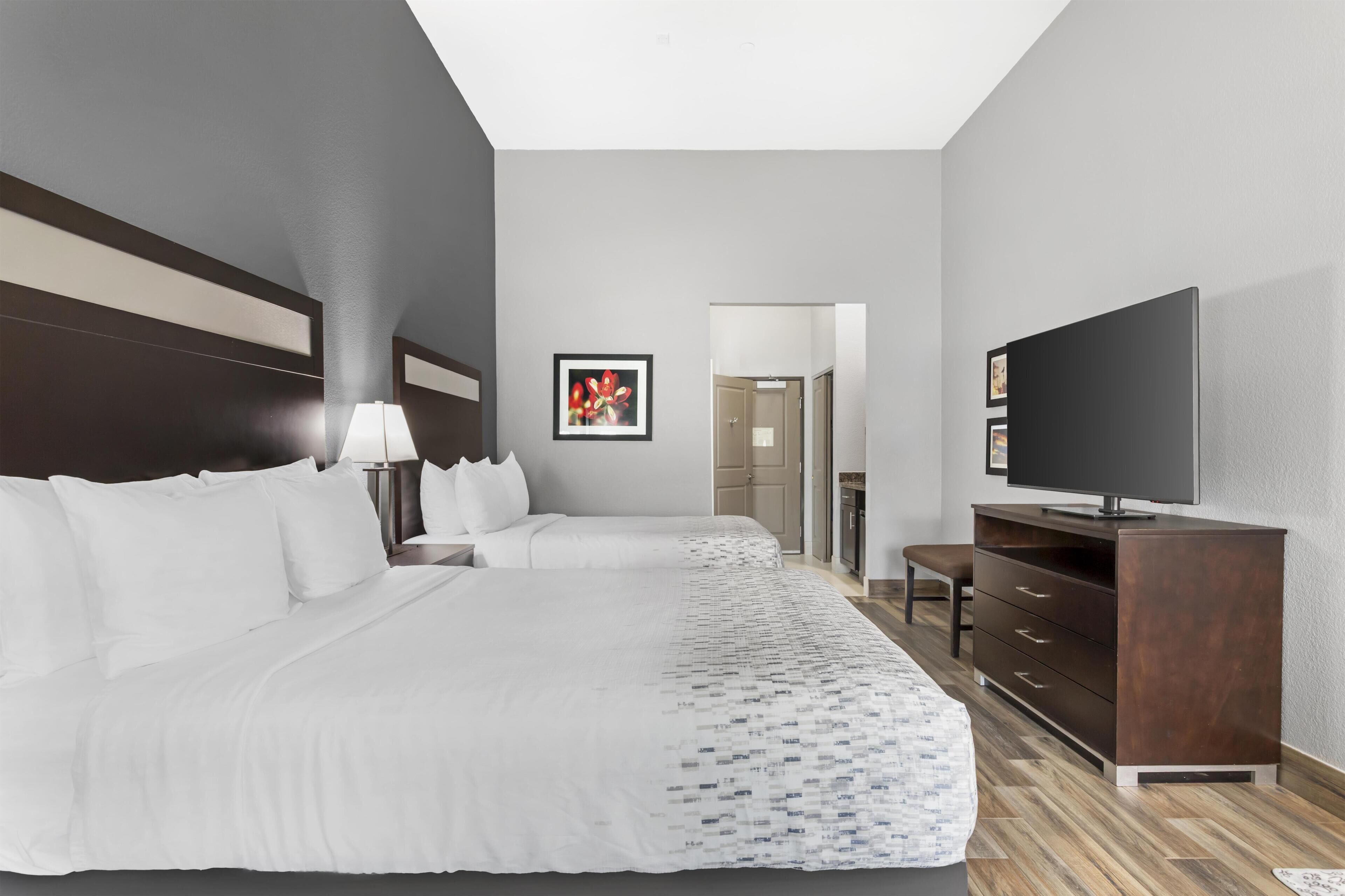 Habitación de hotel con dos camas, televisión, escritorio y puerta que da a un baño.