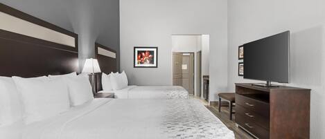Habitación de hotel con dos camas, televisión, escritorio y puerta que da a un baño.