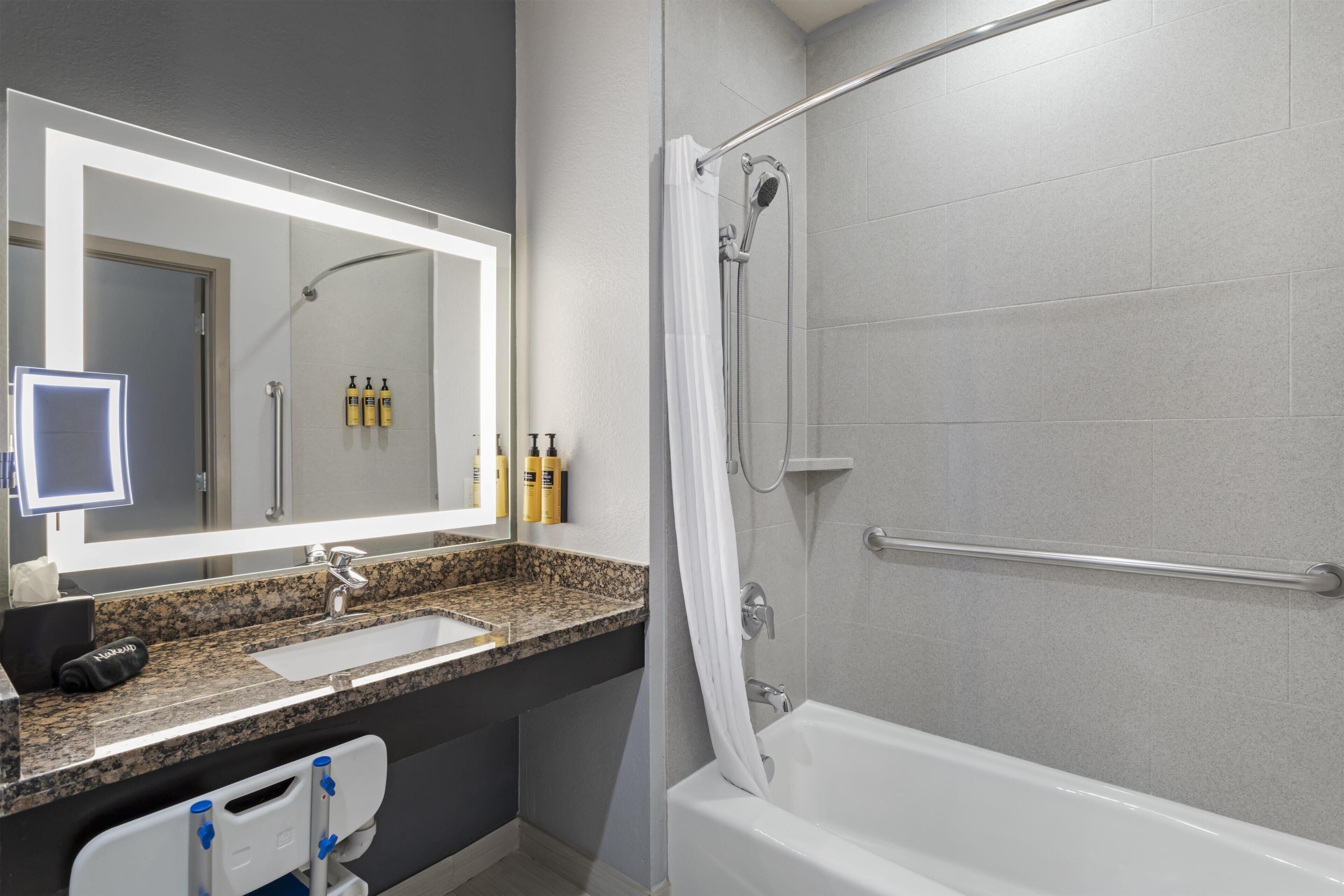 A modern bathroom with a large mirror, a sink, a shower with a glass door, and toiletries on the wall.