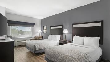 Une chambre d’hôtel avec deux lits, un bureau, une chaise, une fenêtre et un miroir fixé au mur.