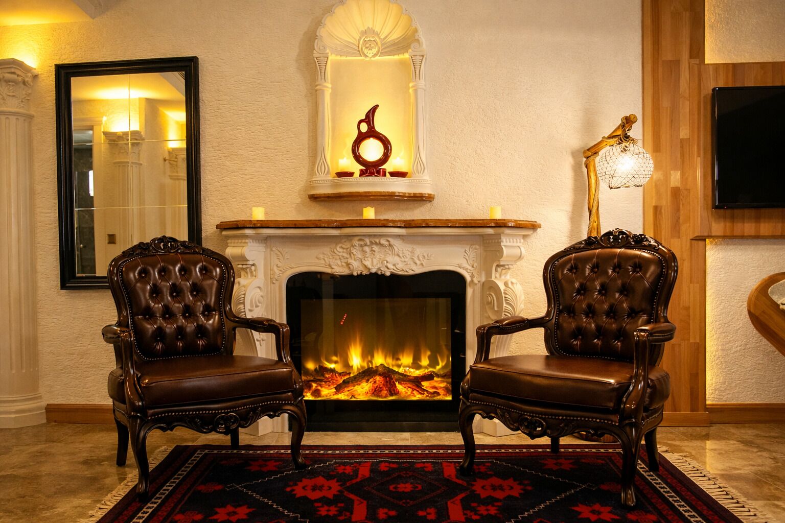 A room with a fireplace, two leather armchairs, a mirror, and a wall-mounted TV.
