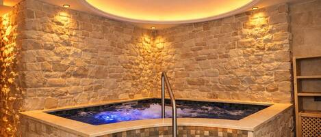 A stone-walled spa area with a hot tub, a metal ladder, and a wooden shelf.