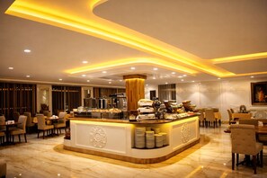 A modern hotel lobby with a central buffet area, seating arrangements, and decorative wall panels.