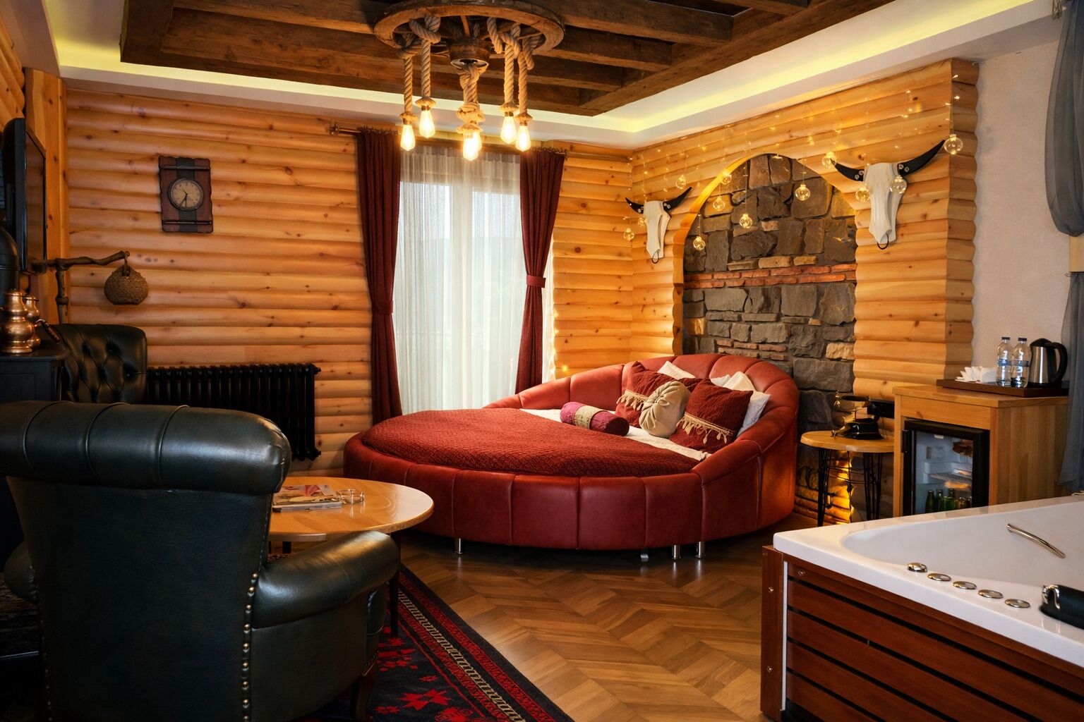 Un dormitorio rústico de cabaña con una cama grande, un sillón de cuero, una mesa de madera y una chimenea de piedra.