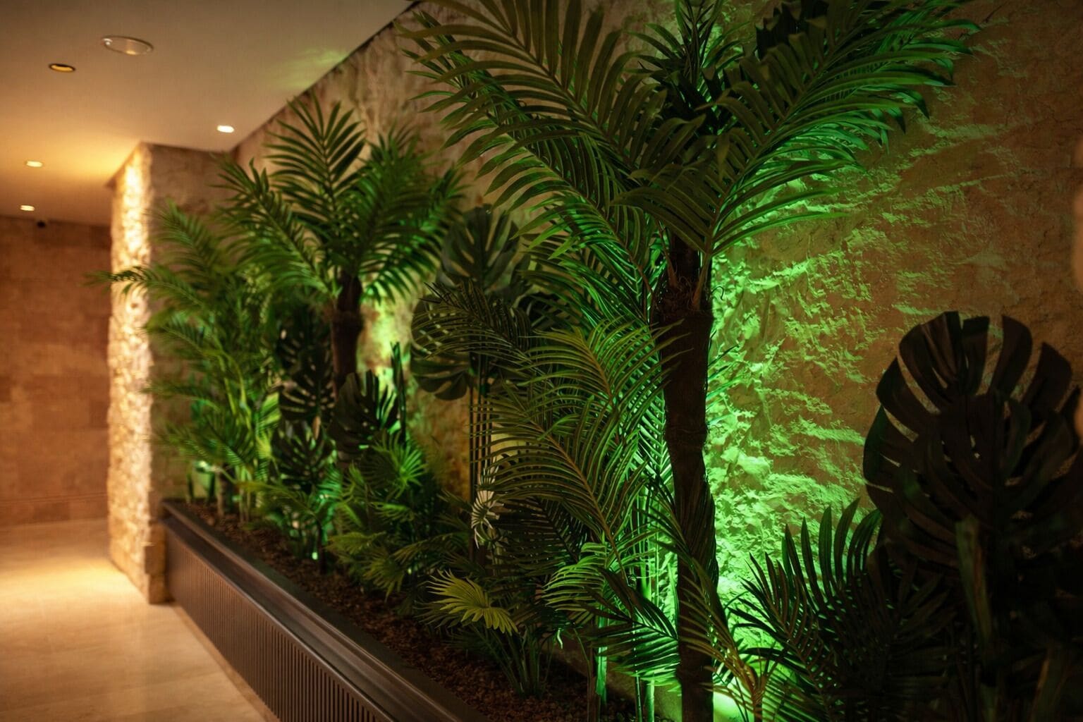 Corredor decorado com plantas tropicais artificiais e um revestimento de parede texturizado.