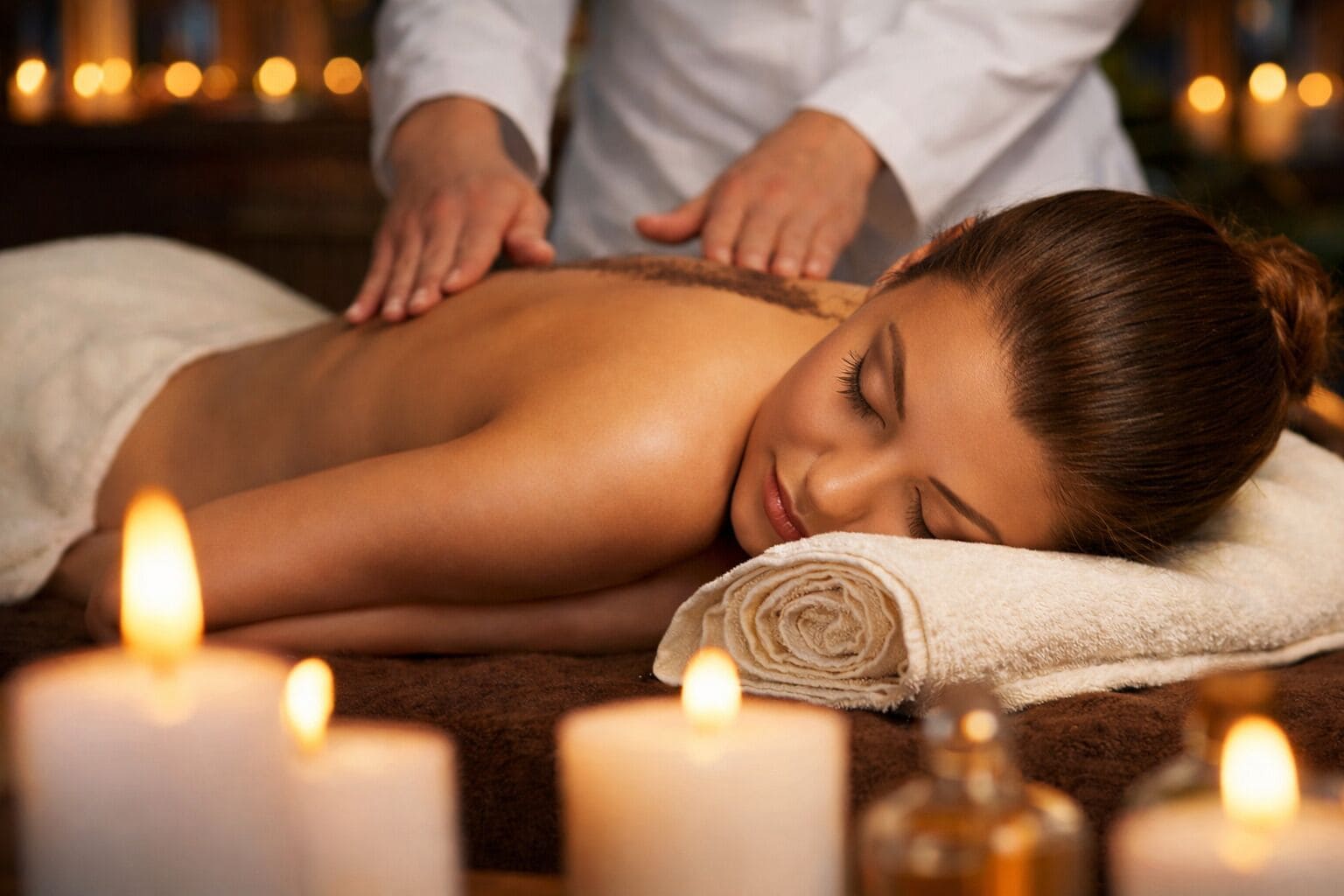 A person receiving a back massage in a spa setting with candles and a towel.