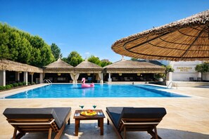 A swimming pool with lounge chairs and a flamingo float, surrounded by thatched-roof structures and a hotel sign. - Emirtimes Hotel & Spa Tuzla (Tuzla)