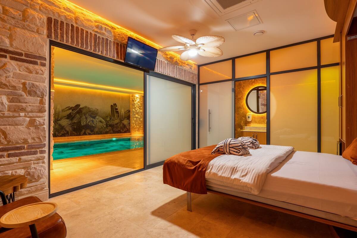 A bedroom with a bed, a view of a pool, and a brick wall.