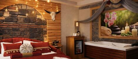A bedroom with a stone wall, a wooden ceiling, a red bed, and a bathroom with a bathtub and a mirror with flowers.