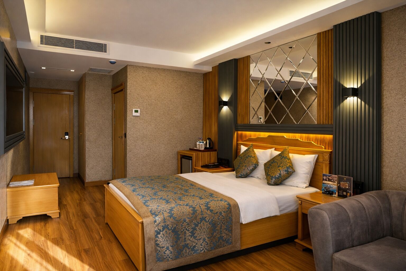 A hotel room with a large bed, a bedside table, a nightstand, a sofa, and a wall-mounted TV.