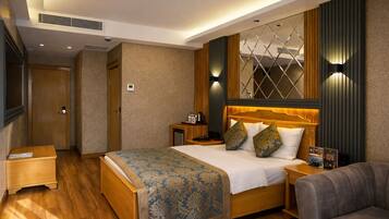 A hotel room with a large bed, a bedside table, a nightstand, a sofa, and a wall-mounted TV.