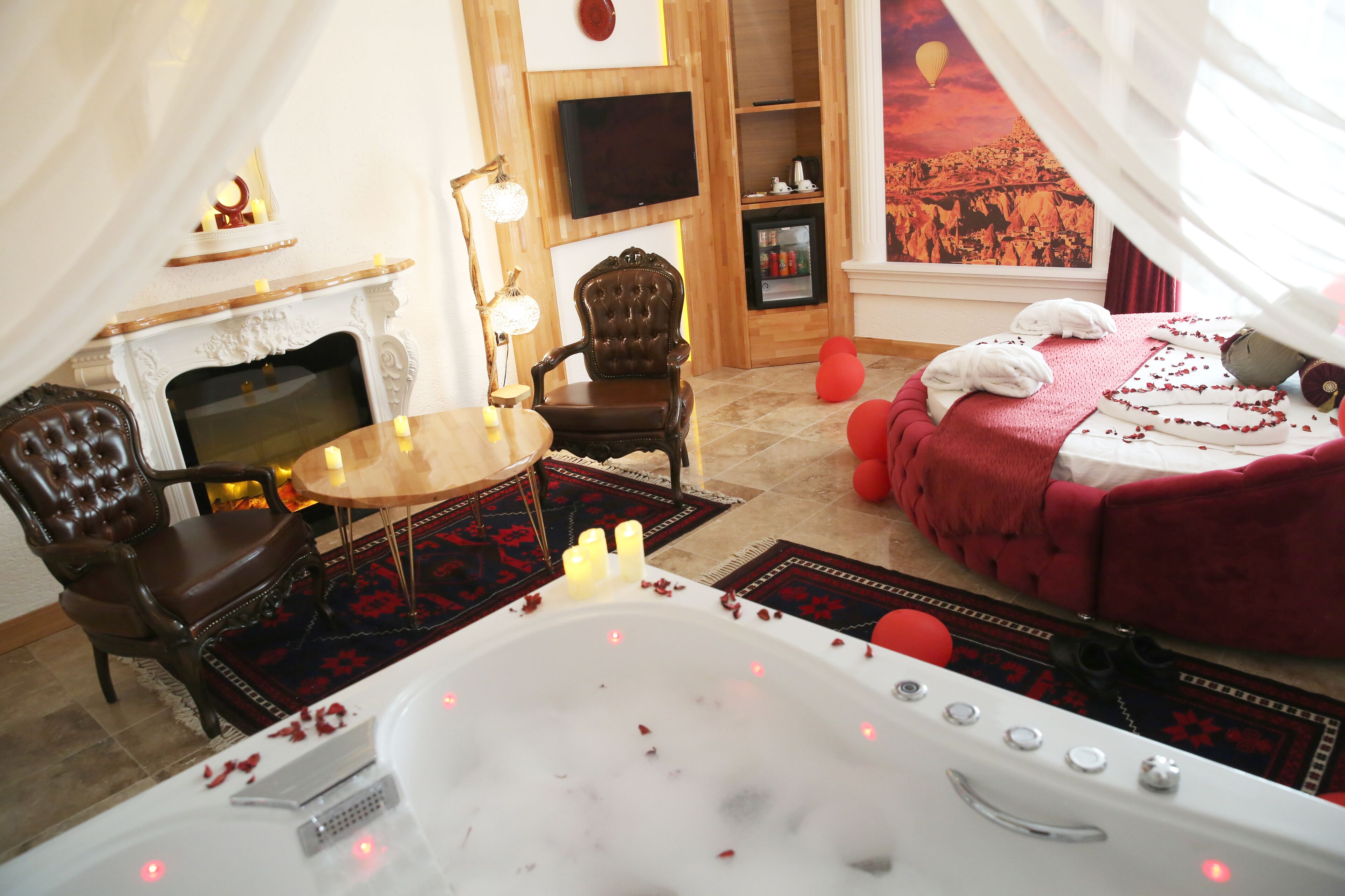 Una habitación lujosa con una bañera grande, una chimenea, un sillón cómodo y una cama acogedora con ropa de cama roja.